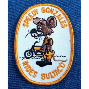 May include: A white oval embroidered patch with an orange border. The patch features a cartoon image of Speedy Gonzales riding a motorcycle with the text "Speedy Gonzales Rides Bultaco" around the image.
