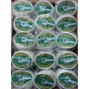 Puede incluir: Un conjunto de parches de Star Trek U.S.S. Enterprise. Cada parche redondo, con fondo verde, presenta el logotipo de Star Trek y una representación de la nave espacial. Los parches están empaquetados individualmente en plástico transparente.