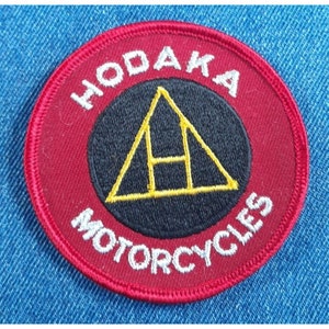 May include: A red and white embroidered patch with the words "HodaKa Motorcycles" and a black and yellow triangle with an "H" inside.