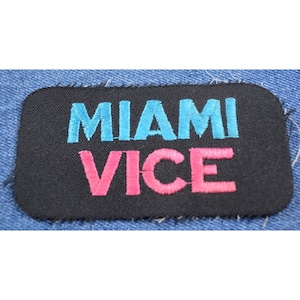 May include: A black fabric patch with the words "Miami Vice" embroidered in blue and pink thread.