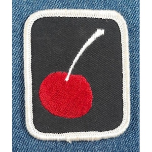 May include: A red cherry with a white stem on a black background. The cherry is surrounded by a white border.