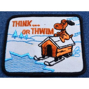 May include: Embroidered patch with a cartoon dog riding a dog house on skis. The text "THINK... OR THWIM" is above the dog. The patch is white with blue and orange accents.