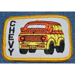 May include: An embroidered iron-on patch featuring a yellow and orange vintage Chevy van with the word "CHEVY" in black lettering on the left side.