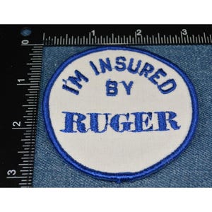 以下が含まれることがあります： 「I'm Insured By Ruger」と青い刺繍で書かれた白い丸いパッチです。
