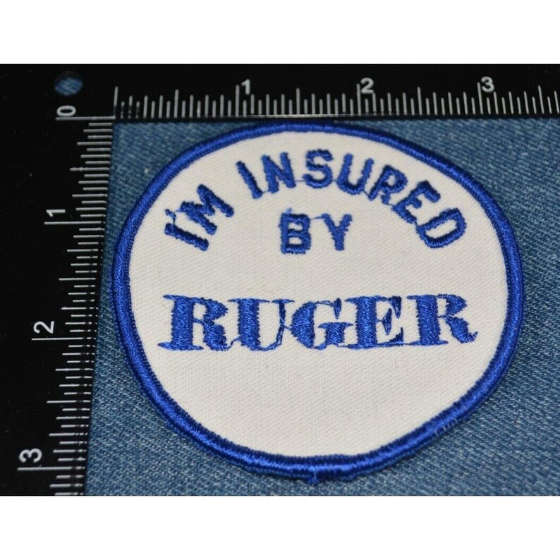以下が含まれることがあります： 「I'm Insured By Ruger」と青い刺繍で書かれた白い丸いパッチです。