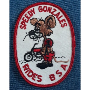 May include: A white embroidered patch with a red border. The patch features a cartoon mouse riding a motorcycle with the text "Speedy Gonzales Rides BSA" around the edge.