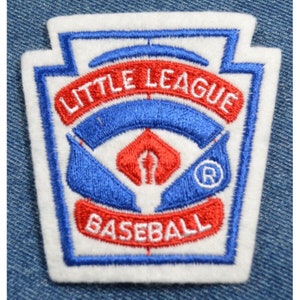 May include: White felt patch with blue and red embroidered details. The patch features the words "Little League Baseball" and a stylized baseball diamond with a bat and ball.