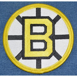 May include: A yellow and black embroidered patch with a large letter "B" in the center. The letter is surrounded by a black and white circle with a black cross in the center.