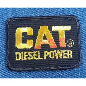 May include: Black embroidered patch with the word "CAT" in yellow and red lettering and the words "Diesel Power" in yellow lettering.