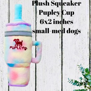 May include: A plush squeaker toy shaped like a cup, featuring a tie-dye pattern in pastel pink, blue, and yellow. The text reads Plush Squeaker Pupley Cup 6x2 inches small-med dogs. It includes a handle, a straw-like top, and a red dog logo.