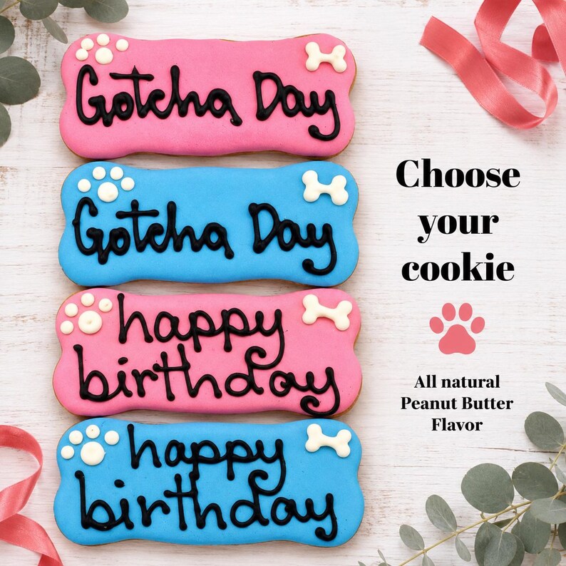 May include: Four bone-shaped dog cookies with pink or blue icing and black lettering. Two cookies read Gotcha Day and two read happy birthday. Text on the right reads Choose your cookie and All natural Peanut Butter Flavor with a paw print.