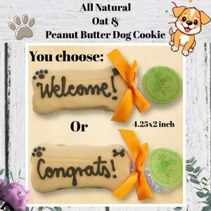May include: An image of dog cookies. The bone-shaped cookies are inscribed with "Welcome!" or "Congrats!" in dark icing. Each cookie is tied with an orange ribbon and accompanied by a small, round, green-labeled treat. The cookies measure 4.25x2 inches.