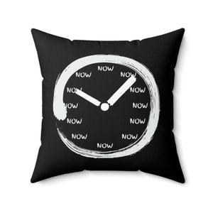 May include: Black throw pillow with a white clock face design. The clock face has the word "NOW" written around the edge and a white hand pointing to the center.