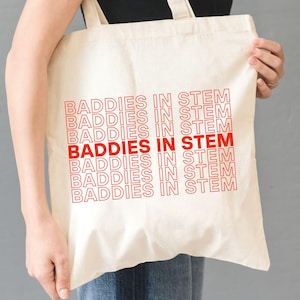 May include: A white tote bag with the phrase "BADDIES IN STEM" repeated in red text.