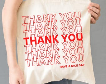 May include: A white canvas tote bag with the phrase "THANK YOU" repeated in red text, with the words "HAVE A NICE DAY" at the bottom.