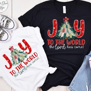 May include: Two t-shirts, one white and one black, with a Christmas tree design. The text "JOY TO THE WORLD the Lord has come!" is printed in red. The white shirt is knotted at the waist, and a pair of leopard print sneakers are visible.