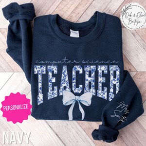 May include: Navy blue sweatshirt with a white floral design and the text "computer science teacher" with a white bow. The text "Miss Smith" is written in the bottom right corner.