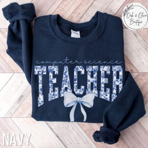 May include: Navy blue sweatshirt with a white floral design that says "computer science teacher" with a white bow.