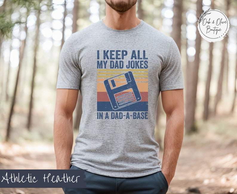 May include: A heather gray t-shirt with a retro-style graphic of a floppy disk and the text "I keep all my dad jokes in a dad-a-base".