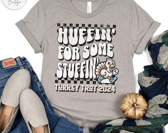 May include: A heather grey t-shirt with a black and white checkered design. The shirt features the text "Huffin' for some stuffin' Turkey Trot 2024" and a cartoon turkey.