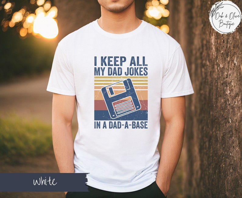 May include: White t-shirt with a retro-style graphic of a floppy disk and the text "I keep all my dad jokes in a dad-a-base".