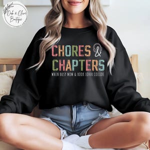 May include: A black sweatshirt with the text "Chores & Chapters" in colorful letters. The text is surrounded by a colorful border and the words "When Busy Mom & Book Lover Collide" are printed below.
