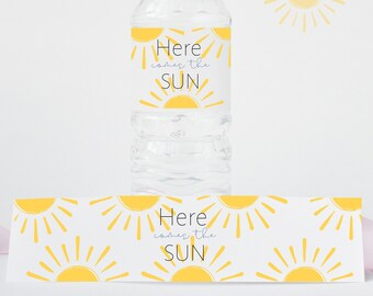 May include: Water bottle label with a yellow sun and the text "Here comes the sun". The label is on a clear plastic water bottle. There is a second label with the same design, but it is longer and has multiple suns.