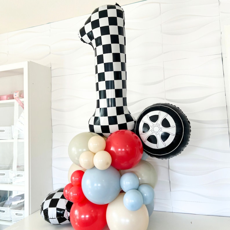 May include: A black and white checkered number one balloon with a black and white tire balloon and a cluster of colorful balloons in red, blue, white, and cream.