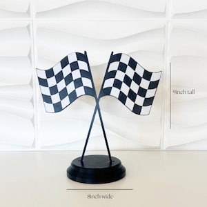 May include: A decorative tabletop display featuring two crossed checkered racing flags in black and white, mounted on a circular black base. The structure measures 9 inches tall and 8 inches wide, with clear text labels indicating these dimensions.