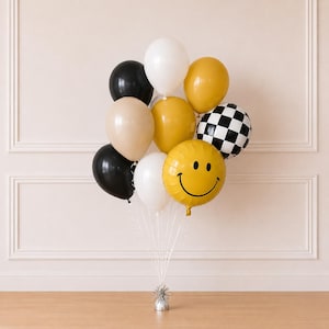 May include: A balloon bouquet featuring a mix of black, white, beige, and mustard yellow latex balloons, alongside a black and white checkered foil balloon and a round yellow foil balloon with a black printed smiley face, all anchored by a silver weight.
