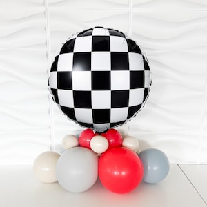 May include: A balloon arrangement featuring a large, round black and white checkered balloon at the top. Below are several smaller balloons in red, white, gray, and blue. This festive arrangement is suitable for a racing-themed party or event.