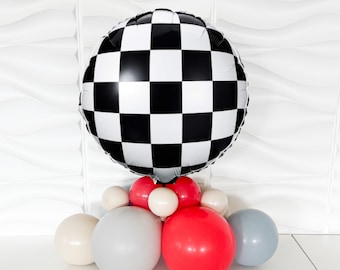 Puede incluir: Un arreglo de globos con un gran globo redondo a cuadros en blanco y negro en la parte superior. Debajo hay varios globos más pequeños en rojo, blanco, gris y azul. Este arreglo festivo es adecuado para una fiesta o evento temático de carreras.