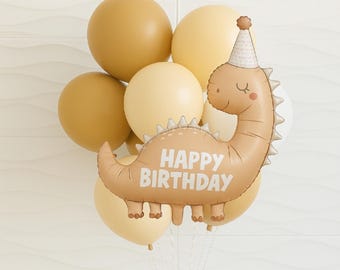 Pode incluir: Um buquê de balões em tons de bege e creme, com um balão em forma de dinossauro que diz "Happy Birthday". O balão de dinossauro tem um chapéu de festa e é cercado por balões redondos.