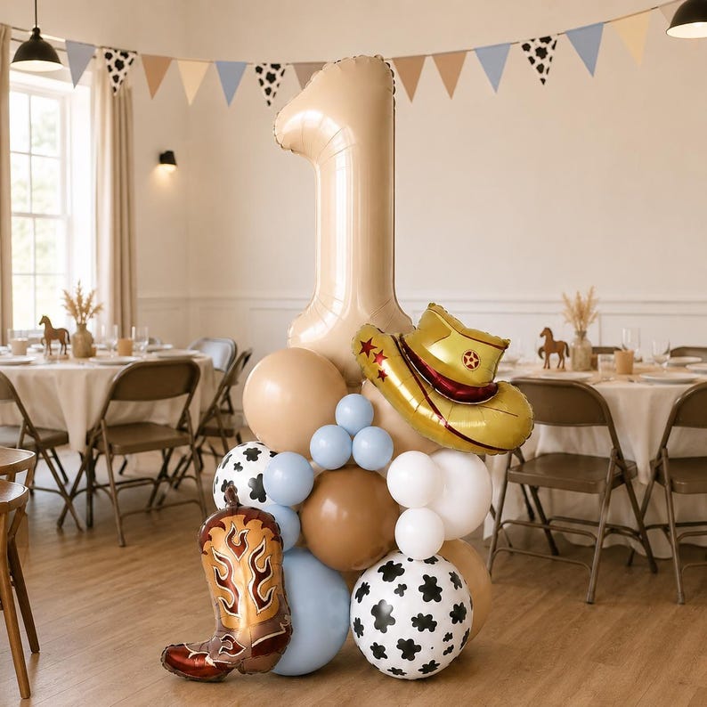 May include: A balloon arrangement featuring a large beige number one balloon, a gold cowboy hat balloon, and a brown cowboy boot balloon. The cluster includes round balloons in beige, light blue, white, and white with black cow print patterns.