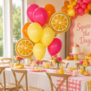 May include: A balloon bouquet featuring bright pink, orange, and yellow latex balloons mixed with two round foil balloons printed with a citrus orange slice pattern. The balloons are tied together with white ribbons, creating a vibrant display.