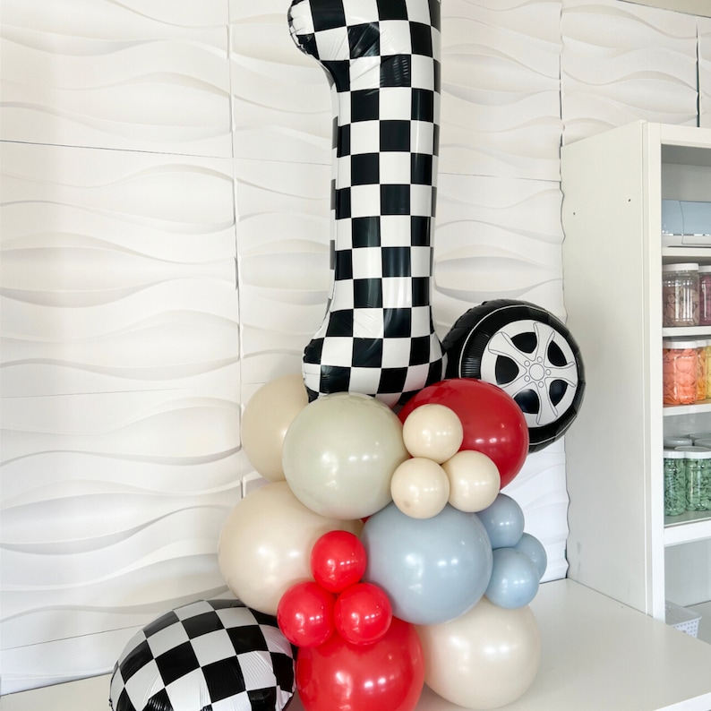 May include: A black and white checkered number one balloon with a black tire balloon and a cluster of balloons in various colors, including red, white, blue, and beige.
