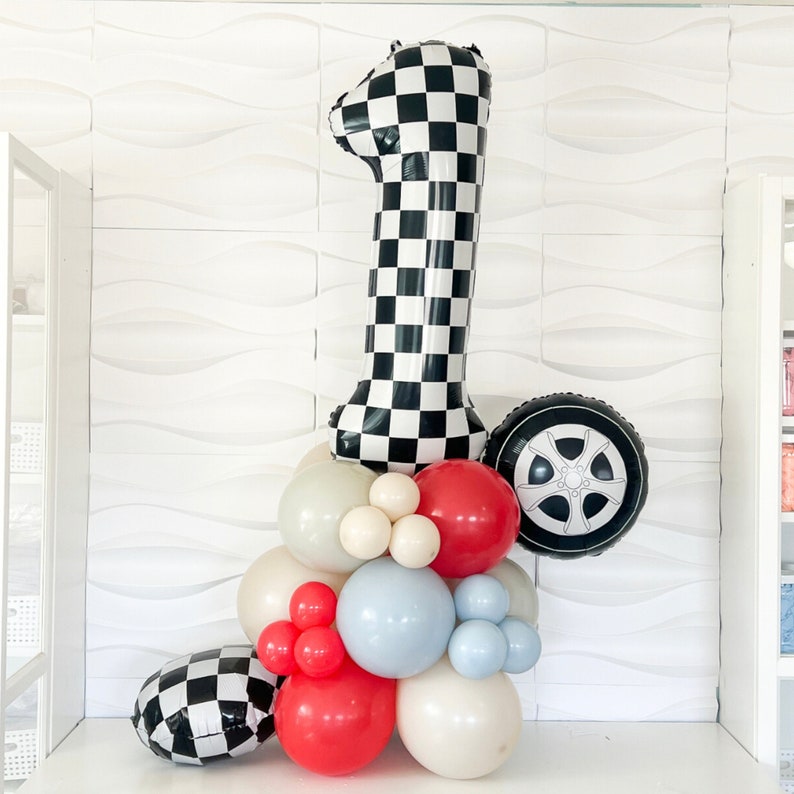 May include: A black and white checkered number one balloon with a black and white tire balloon and a cluster of balloons in red, white, and blue.