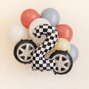 Può includere: Un'allegra composizione di palloncini con un grande numero 2 a scacchi bianchi e neri, che ricorda una bandiera da corsa. La composizione include palloncini rossi, bianchi e grigi, insieme a due palloncini a forma di pneumatico, perfetti per un compleanno.