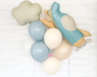Puede incluir: Un globo de avión azul y amarillo con un globo de nube beige y globos redondos azules, beige y blancos.