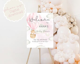 Puede incluir: Un globo aerostático rosa y blanco con un osito de peluche en la cesta. El globo flota en el cielo con nubes. El texto "Bienvenido al Baby Shower de Anna" está escrito en el cartel. El texto "¡Arriba, arriba y lejos! ¡Una niña está en camino!" está escrito debajo del globo.