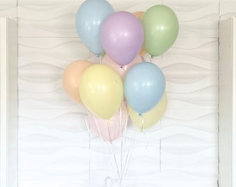 May include: A bouquet of pastel colored balloons tied together with white ribbon. The balloons are light blue, lavender, yellow, peach, and green.