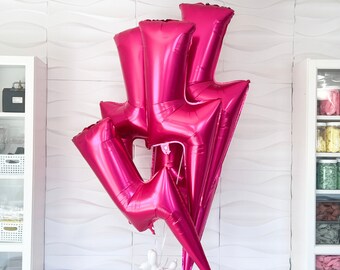 May include: Three large pink lightning bolt shaped balloons. The balloons are arranged in a stack with the largest balloon at the bottom and the smallest balloon at the top.