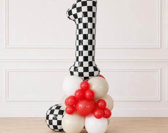 May include: A large number one shaped foil balloon with a black and white checkered pattern, anchored by a cluster of round latex balloons in solid red, white, and beige, with an additional black and white checkered sphere balloon at the base.