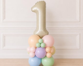 May include: A large beige number one foil balloon standing atop a cluster of smaller latex balloons in pastel shades of peach, pink, lavender, light blue, mint green, and pale yellow, arranged in a decorative column formation for display.