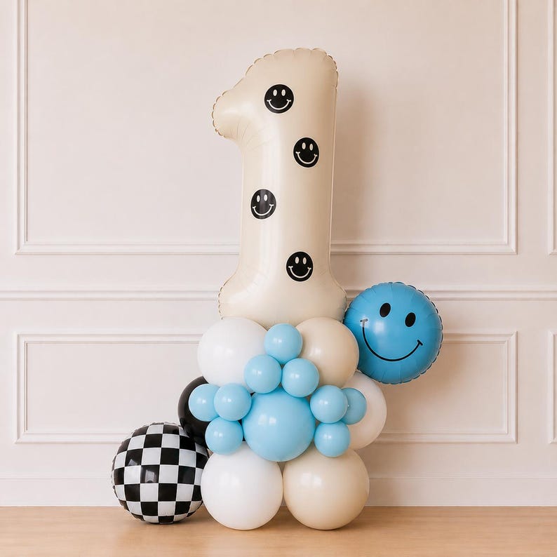 Pu&ograve; includere: Un grande palloncino a forma di numero uno color crema decorato con faccine sorridenti nere, circondato da un gruppo di palloncini bianchi, crema e azzurri, un palloncino rotondo blu con faccina sorridente e un palloncino sferico a scacchi.
