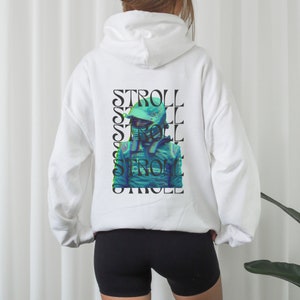 Op de afbeelding: Witte hoodie met een grafische print van een raceautocoureur met een helm. De grafiek wordt verticaal herhaald met het woord "STROLL" in zwarte tekst.