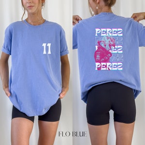 May include: A light blue t-shirt with the number "11" printed on the front and a graphic of a race car driver with the name "Perez" repeated in a layered effect on the back.