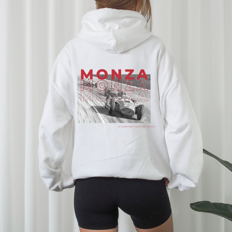 May include: White hooded sweatshirt with a black and white image of a vintage race car on the back. The image is surrounded by the word "MONZA" in red text. The text "AUTODROMO NAZIONALE MONZA" is printed below the image.