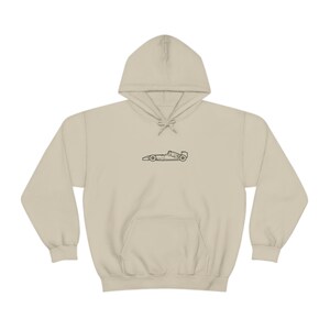 May include: A beige hoodie with a black outline of a racing car on the front.