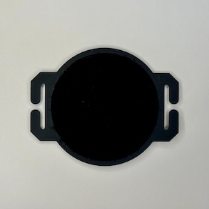 May include: A black, circular object with a central dark circle and four rectangular tabs extending outwards. The object is set against a white background, highlighting its shape and design. The tabs appear to be for attachment.